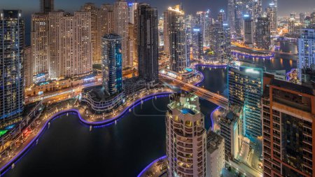 Téléchargez les photos : Vue de différents gratte-ciel dans le plus haut bloc recidential de Dubai Marina et le quartier JBR transition aérienne de jour à la nuit avec canal artificiel. Nombreuses tours et yachts après le coucher du soleil - en image libre de droit