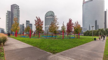 Téléchargez les photos : Panorama showing skyscrapers and biblioteca from park with green lawn and orange trees timelapse. Located between Piazza Gae Aulenti and Isola district. Traffic on a road intersection. Milan. Italy - en image libre de droit