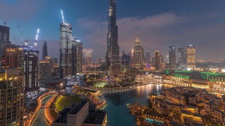 Téléchargez les photos : Gratte-ciel s'élevant au-dessus du centre-ville de Dubaï transition de jour à la nuit, centre commercial et fontaine entourés de bâtiments modernes vue panoramique aérienne avec ciel nuageux coloré - en image libre de droit