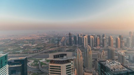 Téléchargez les photos : Panorama of Dubai Marina with JLT skyscrapers and golf course during sunset, Dubai, United Arab Emirates. Aerial view from above towers. City skyline with rooftops - en image libre de droit