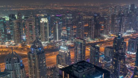 Téléchargez les photos : JLT et Dubai gratte-ciel de la marina près de Sheikh Zayed Road jour à nuit transition aérienne. Bâtiments résidentiels éclairés et circulation routière - en image libre de droit