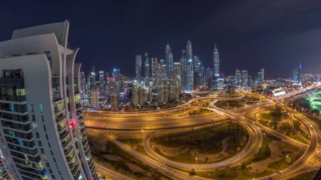 Foto de Panorama de Dubai Marina después del atardecer intersección carretera espagueti cruce día a noche transición. Rascacielos más altos iluminados sobre un fondo. Vista aérea desde el distrito JLT. - Imagen libre de derechos