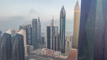 Foto de Centro financiero de la ciudad de Dubai con rascacielos de lujo iluminados noche a día transición, Dubai, Emiratos Árabes Unidos. Vista aérea con parking y torres en los tejados - Imagen libre de derechos