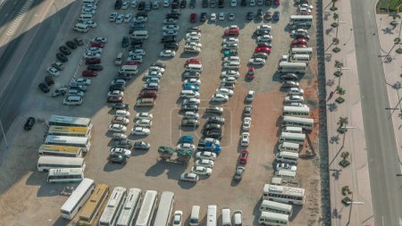 Téléchargez les photos : Vue aérienne d'un parking avec de nombreuses voitures et bus en rangées toute la journée avec des ombres se déplaçant rapidement. Espace libre sur un sable - en image libre de droit