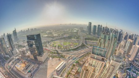 Foto de Panorama del amanecer sobre el puerto deportivo de Dubái y los rascacielos JLT a lo largo de la mañana aérea Sheikh Zayed Road. Edificios residenciales y de oficinas en la ciudad de medios de comunicación desde arriba. Cielo naranja sobre campo de golf - Imagen libre de derechos