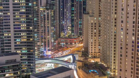 Téléchargez les photos : Vue d'ensemble de JBR et Dubai Marina skyline avec gratte-ciel modernes gratte-ciel front de mer vivant appartements aérien jour à nuit transition. Trafic routier à l'intersection et passerelle - en image libre de droit