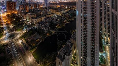 Téléchargez les photos : Bâtiments d'étang et de faible hauteur dans le quartier des Verts pendant toute la nuit. Skyline de Dubaï avec des gratte-ciel dans le quartier de Barsha Heights sur un fond - en image libre de droit