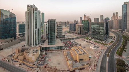 Téléchargez les photos : Business Bay Dubai illuminé gratte-ciel avec canal d'eau aérienne nuit à jour transition panoramique. Aménagement à usage mixte avec tours résidentielles et bureaux partageant également l'empreinte - en image libre de droit