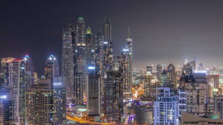 Téléchargez les photos : Vue de différents gratte-ciel dans le plus haut bloc recidential de Dubai Marina transition aérienne de jour à la nuit avec canal artificiel. Nombreuses tours et yachts après le coucher du soleil - en image libre de droit