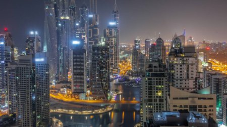 Foto de Vista de varios rascacielos en el bloque recidencial más alto de Dubai Marina aérea durante la noche con canal artificial. Muchas torres con luces apagadas - Imagen libre de derechos