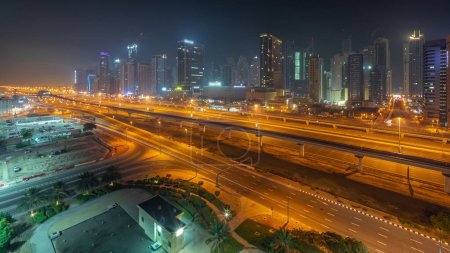 Téléchargez les photos : Dubai Marina gratte-ciel et Sheikh Zayed route avec métro ferroviaire panoramique aérienne pendant toute la nuit. Trafic sur une autoroute près des tours modernes, Émirats arabes unis - en image libre de droit