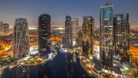 Téléchargez les photos : Bâtiments résidentiels hauts du quartier JLT transition aérienne du jour à la nuit panoramique, faisant partie du quartier mixte du centre multi-commodités de Dubaï. Villa maisons sur un fond - en image libre de droit