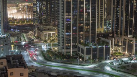 Foto de Vista aérea del tráfico urbano del centro de Dubái con fuente y muchas torres iluminadas durante la noche. Área de negocios en la ciudad urbana inteligente. Rascacielos y edificios de gran altura desde arriba, Emiratos Árabes Unidos. - Imagen libre de derechos