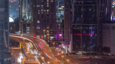 Foto de Vista aérea superior de la concurrida intersección de carreteras y cruces en Dubai City Night Timelapse. Diseño moderno de construcción de encrucijadas y autopistas para evitar atascos de tráfico. Coches cerca de rascacielos bahía de negocios - Imagen libre de derechos