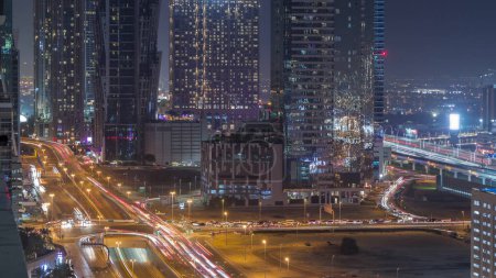 Foto de Skyline distrito de la bahía de negocios con la arquitectura moderna timelapse noche desde arriba. Tráfico en un cruce. Vista aérea de los rascacielos y torres iluminadas de Dubái cerca de la carretera principal. - Imagen libre de derechos