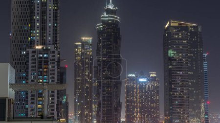 Foto de Skyline distrito de la bahía de negocios con la arquitectura moderna timelapse noche desde arriba. Vista aérea de los rascacielos y torres iluminadas de Dubái cerca de la carretera principal. Cielo oscuro - Imagen libre de derechos