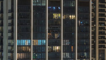 Téléchargez les photos : Grands blocs d'appartements avec fenêtres lumineuses situés dans le nouveau quartier résidentiel de la ville timelapse aérien. Lumière du soir dans les chambres des tours et des gratte-ciel - en image libre de droit