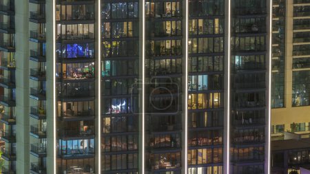 Téléchargez les photos : Grands blocs d'appartements avec des fenêtres panoramiques lumineuses situés dans le quartier résidentiel de la ville timelapse aérien. Lumière du soir dans les chambres des tours et des gratte-ciel - en image libre de droit