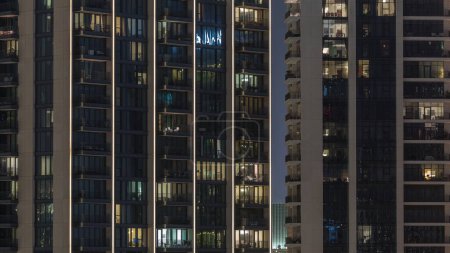 Téléchargez les photos : Lumière du soir dans les chambres des tours et des gratte-ciel. Grands blocs d'appartements avec fenêtres lumineuses situés dans le quartier résidentiel de la ville timelapse aérienne. - en image libre de droit