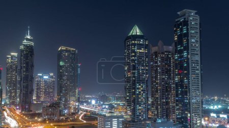 Téléchargez les photos : Business Bay skyline de quartier avec l'architecture moderne timelapse pendant toute la nuit d'en haut. Vue aérienne des gratte-ciel de Dubaï avec des fenêtres clignotantes et des tours éclairées près de la circulation routière principale - en image libre de droit