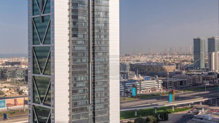 Téléchargez les photos : Vue aérienne vers Dubai City Walk district vu derrière gratte-ciel timelapse. Arena, bâtiments de faible hauteur et villas créées comme des rues de style européen. Trafic sur la route cheikh zayed et la ligne de métro - en image libre de droit