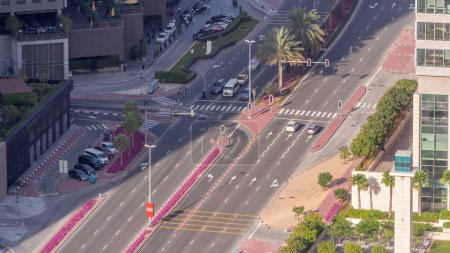 Photo for Aerial view from above to a busy road intersection in Dubai timelapse. Colorful cars and trucks driving straight forward in both directions and pedestrians crossing the road. Financial district - Royalty Free Image