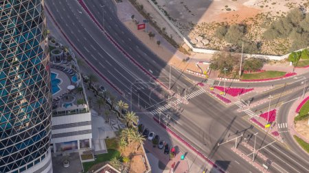 Photo for Aerial view from above to a busy road intersection in Dubai timelapse. Colorful cars driving straight forward in both directions and pedestrians crossing the road. Financial district with parking lot - Royalty Free Image