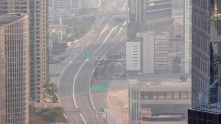 Téléchargez les photos : Vue aérienne d'en haut à un carrefour routier animé dans le centre-ville de Dubaï timelapse. Voitures et camions conduisant directement dans les deux sens la route entre les gratte-ciel. Temps haineux - en image libre de droit