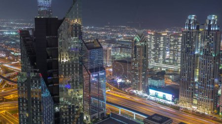 Foto de Edificios de gran altura en Sheikh Zayed Road en Dubai aerial night timelapse, EAU. Rascacielos iluminados en el distrito financiero internacional desde arriba. Casas de paseo por la ciudad y villas en un fondo - Imagen libre de derechos