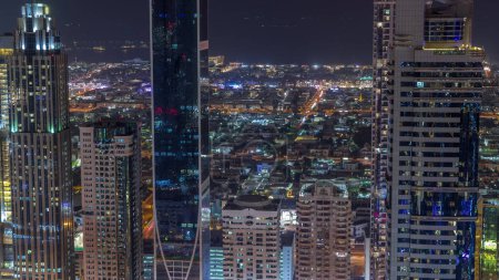 Foto de Vista del horizonte de los edificios de gran altura en Sheikh Zayed Road en Dubai timelapse noche aérea, Emiratos Árabes Unidos. Rascacielos iluminados en el Centro Financiero Internacional desde arriba. Casas de villa detrás - Imagen libre de derechos