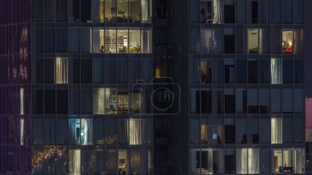 Photo for Frontal view of night facade of tower building with a lot of blinking windows with light timelapse. Life in every window. Aerial view of the glass facade of residential skyscraper. - Royalty Free Image