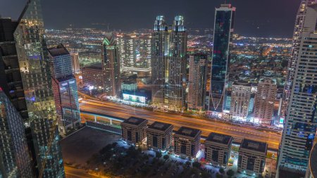Téléchargez les photos : Bâtiments de grande hauteur sur Sheikh Zayed Road à Dubaï timelapse de nuit aérienne, EAU. gratte-ciel dans le quartier financier international d'en haut. Maisons de promenade de la ville sur un fond. Parking près de l'autoroute - en image libre de droit