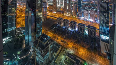 Foto de Edificios de gran altura en Sheikh Zayed Road en Dubai antena noche a día transición panorámica timelapse, Emiratos Árabes Unidos. Rascacielos en el distrito financiero desde arriba. Paseo por la ciudad casas y villas en el fondo - Imagen libre de derechos