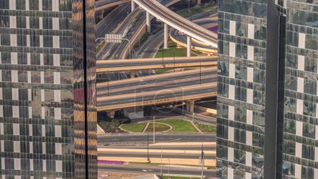 Téléchargez les photos : Vue aérienne entre les gratte-ciel d'en haut à un énorme carrefour routier achalandé avec ligne de métro dans le centre-ville de Dubaï timelapse. Des voitures et des camions colorés conduisant directement dans les deux sens de la route. - en image libre de droit