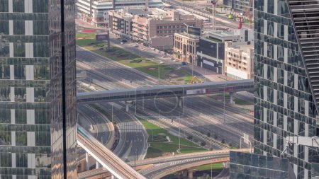 Foto de Vista aérea desde arriba a una concurrida intersección de carreteras en Dubai timelapse centro. Coches coloridos y camiones que conducen en ambas direcciones en la carretera sheikh zayed. Largas sombras de rascacielos - Imagen libre de derechos