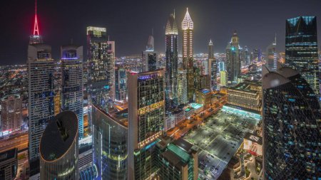 Foto de Panorama que muestra la vista del horizonte de los edificios de gran altura en Sheikh Zayed Road en Dubai timelapse noche aérea, Emiratos Árabes Unidos. Rascacielos iluminados en el Centro Financiero Internacional desde arriba - Imagen libre de derechos