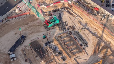 Photo for Aerial view construction site with a foundation pit of new skyscraper timelapse. Earthwork in excavation and backfilling of soil. Heavy machinery for earthmoving with crane unloading truck. - Royalty Free Image