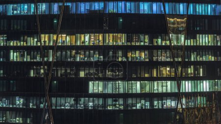 Photo for Frontal view of night facade of tower building with a lot of windows with light timelapse. Life in every window. Aerial view of the glass facade of an office skyscraper in financial district. - Royalty Free Image