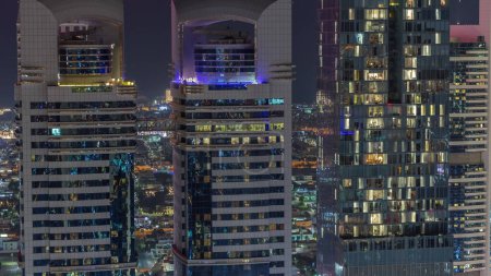 Téléchargez les photos : Skyline vue rapprochée des immeubles de grande hauteur sur Sheikh Zayed Road à Dubaï timelapse de nuit aérienne, Émirats arabes unis. Fenêtres clignotantes dans les gratte-ciel éclairés de la place financière internationale d'en haut - en image libre de droit