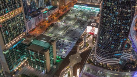 Téléchargez les photos : Vue aérienne du grand parking entouré par les immeubles de grande hauteur sur Sheikh Zayed Road à Dubaï timelapse de nuit aérienne, Émirats arabes unis. Des gratte-ciel éclairés de la place financière internationale d'en haut - en image libre de droit