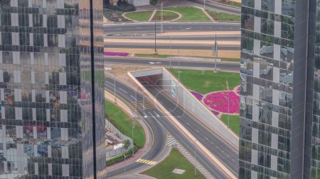 Photo for Aerial view from above to a busy road junction with tunnel in Dubai downtown timelapse. Colorful cars and trucks driving straight forward on highway road. Flowerbed with green lawn between skyscrapers - Royalty Free Image