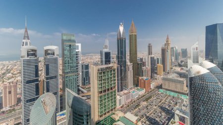 Téléchargez les photos : Pamorama montrant la vue d'horizon des immeubles de grande hauteur sur Sheikh Zayed Road à Dubaï timelapse aérien, Émirats arabes unis. Les gratte-ciel de la place financière internationale d'en haut avec des nuages sur un ciel bleu - en image libre de droit