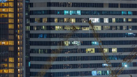 Foto de Edificios de oficinas y residenciales ventanas iluminadas por la noche timelapse. Arquitectura de vidrio, edificio corporativo por la noche con luces brillantes. Grúas en un sitio de construcción en frente - Imagen libre de derechos