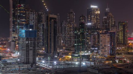 Téléchargez les photos : Paysage urbain avec des gratte-ciel éclairés de Dubai Business Bay et canal d'eau timelapse de nuit aérienne. Skyline moderne avec des tours résidentielles et de bureaux sur le front de mer. Bâtiments en construction - en image libre de droit