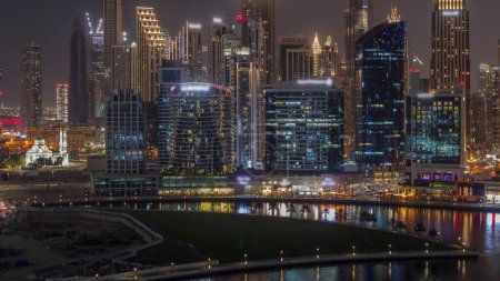 Téléchargez les photos : Vue aérienne vers Dubai Business Bay et le centre-ville avec les différents gratte-ciel et tours éclairés le long du front de mer sur le canal timelapse de nuit. - en image libre de droit
