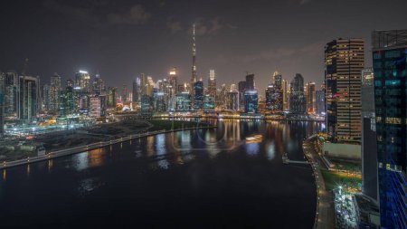 Foto de Panorama que muestra una vista aérea de Dubai Business Bay y el centro de la ciudad con los diversos rascacielos y torres a lo largo de la costa en la noche del canal timelapse. Construcción con grúas - Imagen libre de derechos