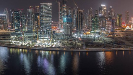 Téléchargez les photos : Paysage urbain avec des gratte-ciel éclairés de Dubai Business Bay et canal d'eau timelapse de nuit aérienne. Skyline moderne avec des tours résidentielles et de bureaux sur le front de mer. Grand chantier et trafic - en image libre de droit