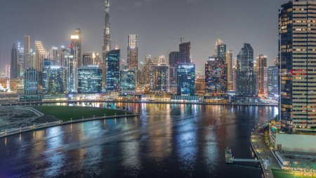 Téléchargez les photos : Vue aérienne vers Dubai Business Bay et le centre-ville avec les différents gratte-ciel et tours le long du front de mer sur le canal timelapse de nuit. Site de construction avec grues. Réflexion dans l'eau - en image libre de droit