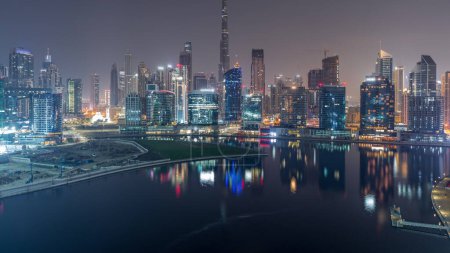 Foto de Vista aérea de Dubai Business Bay y el centro de la ciudad con los diversos rascacielos y torres a lo largo de la costa en el canal noche a día timelapse transición. Lugar de construcción con grúas antes del amanecer - Imagen libre de derechos