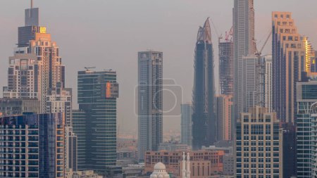 Téléchargez les photos : Paysage urbain avec des gratte-ciel de Dubai Business Bay matin aérien timelapse. Skyline moderne avec mosquée entourée de tours résidentielles et de bureaux au lever du soleil. Lumière chaude et ombres longues - en image libre de droit